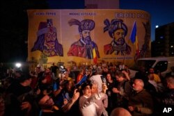 Сторонники Джордже Симиона реагируют на результаты экзитполов на фоне изображений румынских исторических фигур у штаб-квартиры Альянса за объединение румын (AUR) после закрытия избирательных участков в первом туре повторных президентских выборов в Бухаресте, 4 мая 2025 года